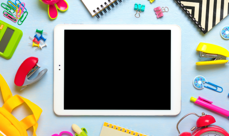 Image of a blank tablet with various objects next to it: staplers, scissors, paperclips, and pens