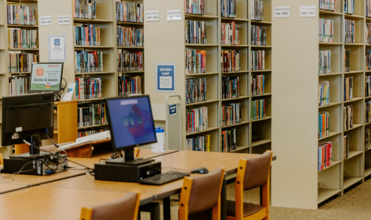 Image of computer on table and bookshelves in the library.